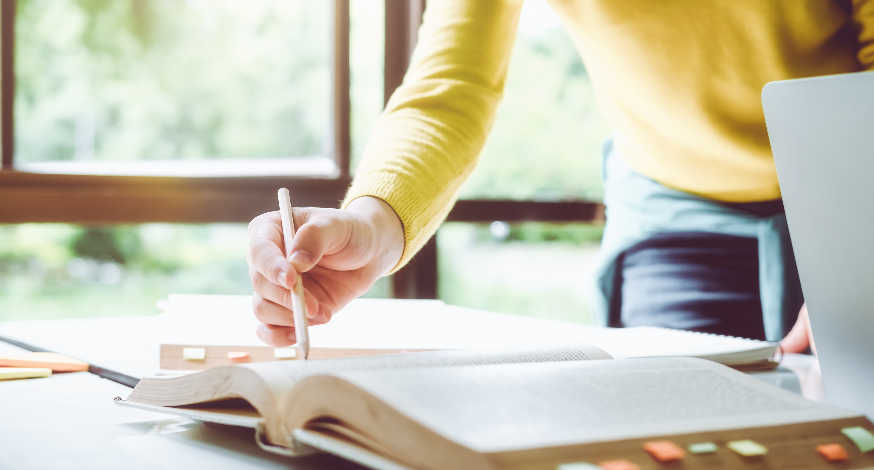 Person writing in a large planner open on table with colourful sticky notes 