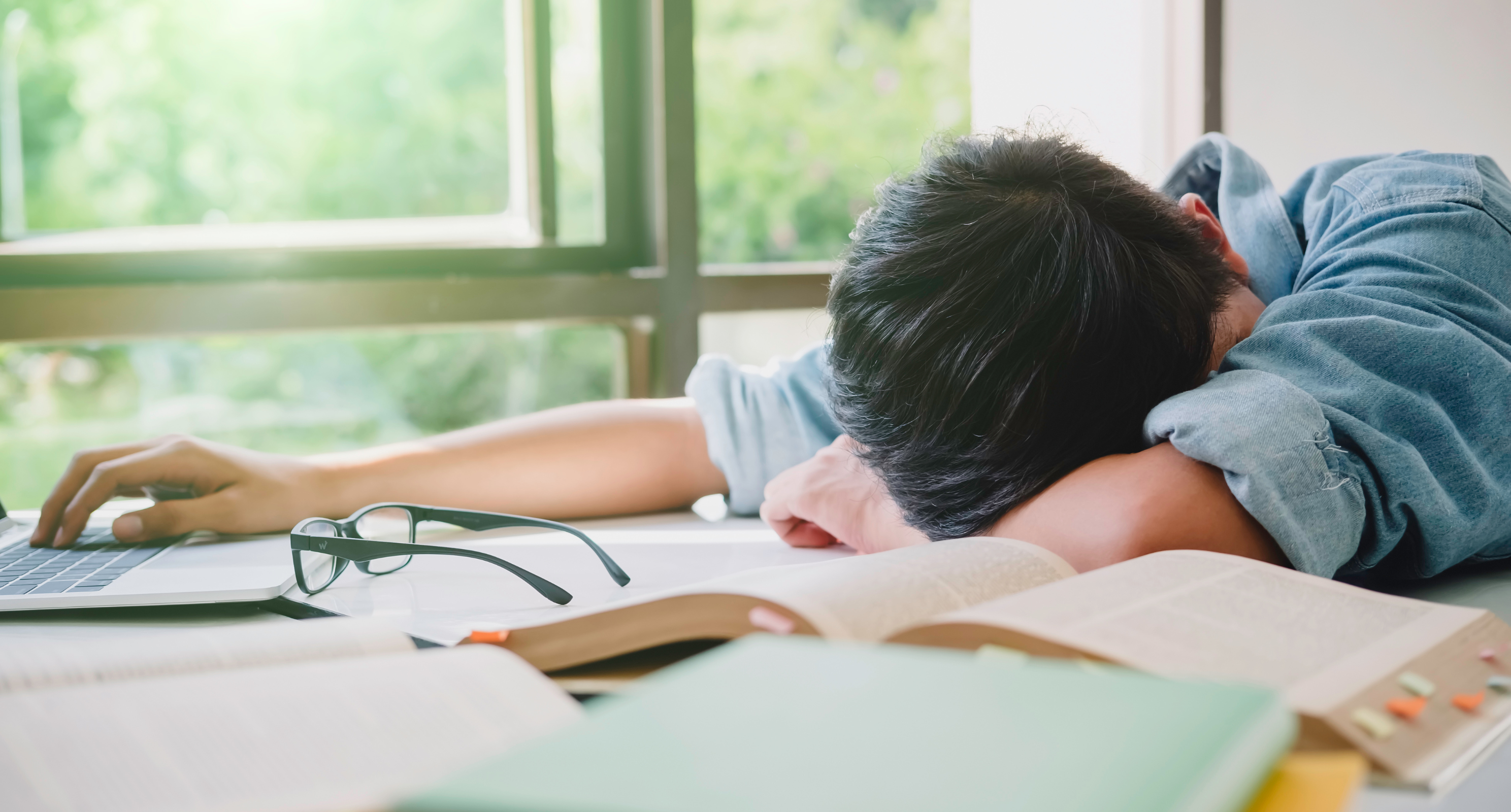 Teen in despair with head collapsed over books on table