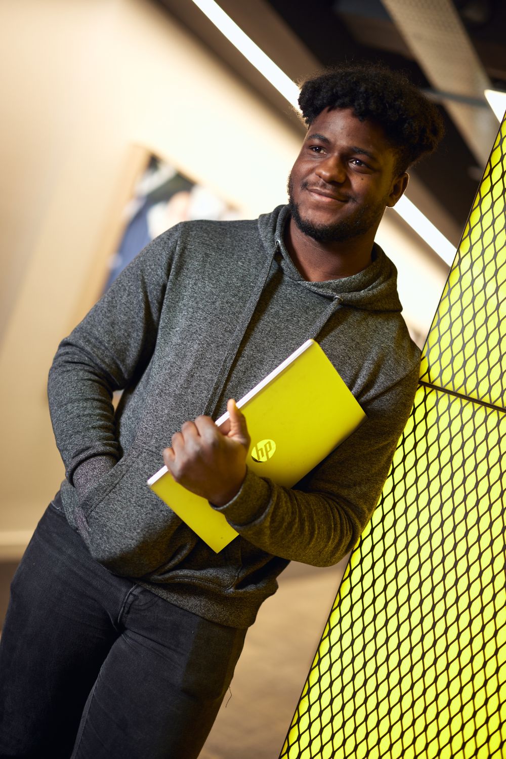 A young man wearing a hoodie smiles while holding a laptop, showcasing his readiness and enthusiasm.