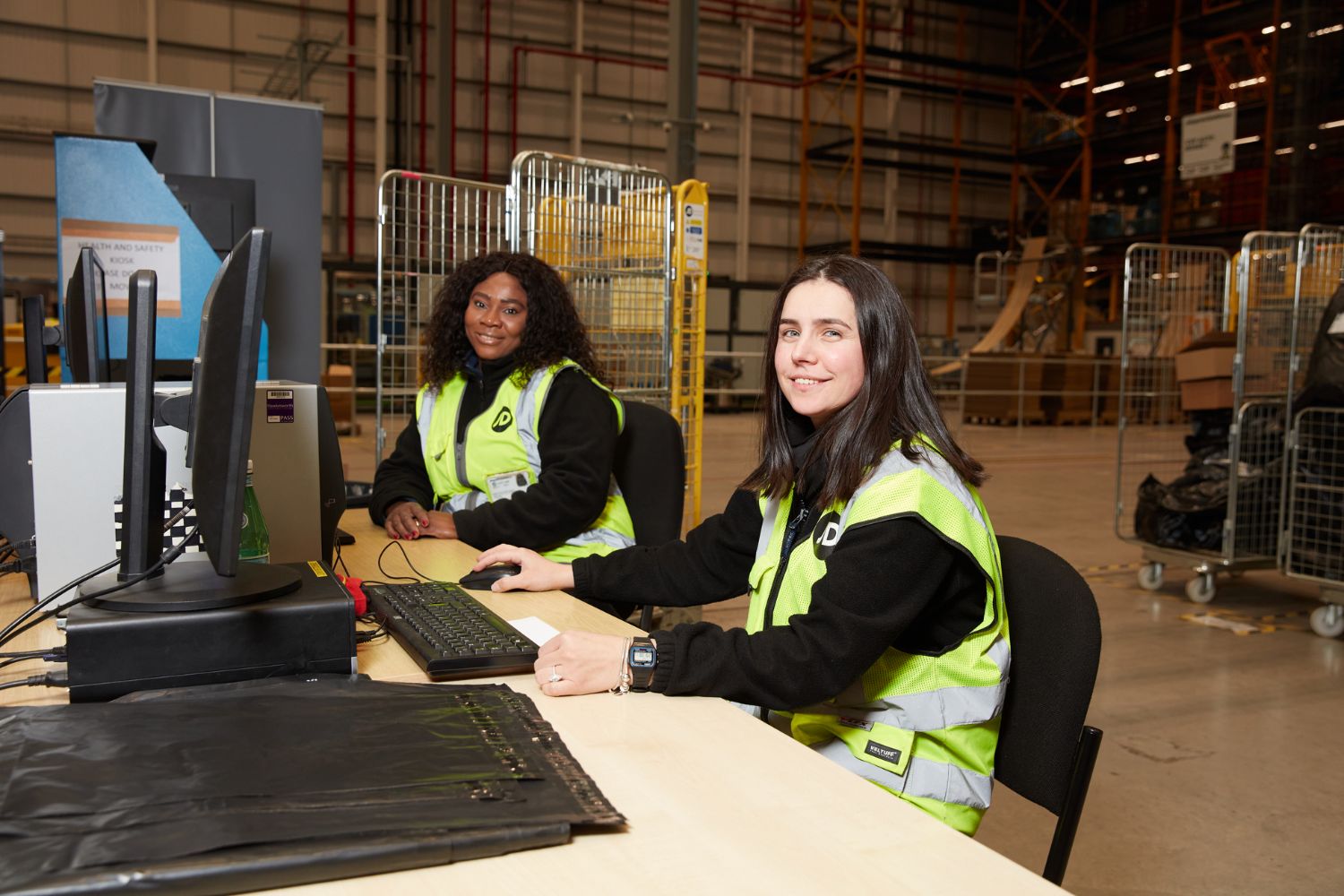 Two women wearing safety vests engage in teamwork at a desk, surrounded by documents and office materials.