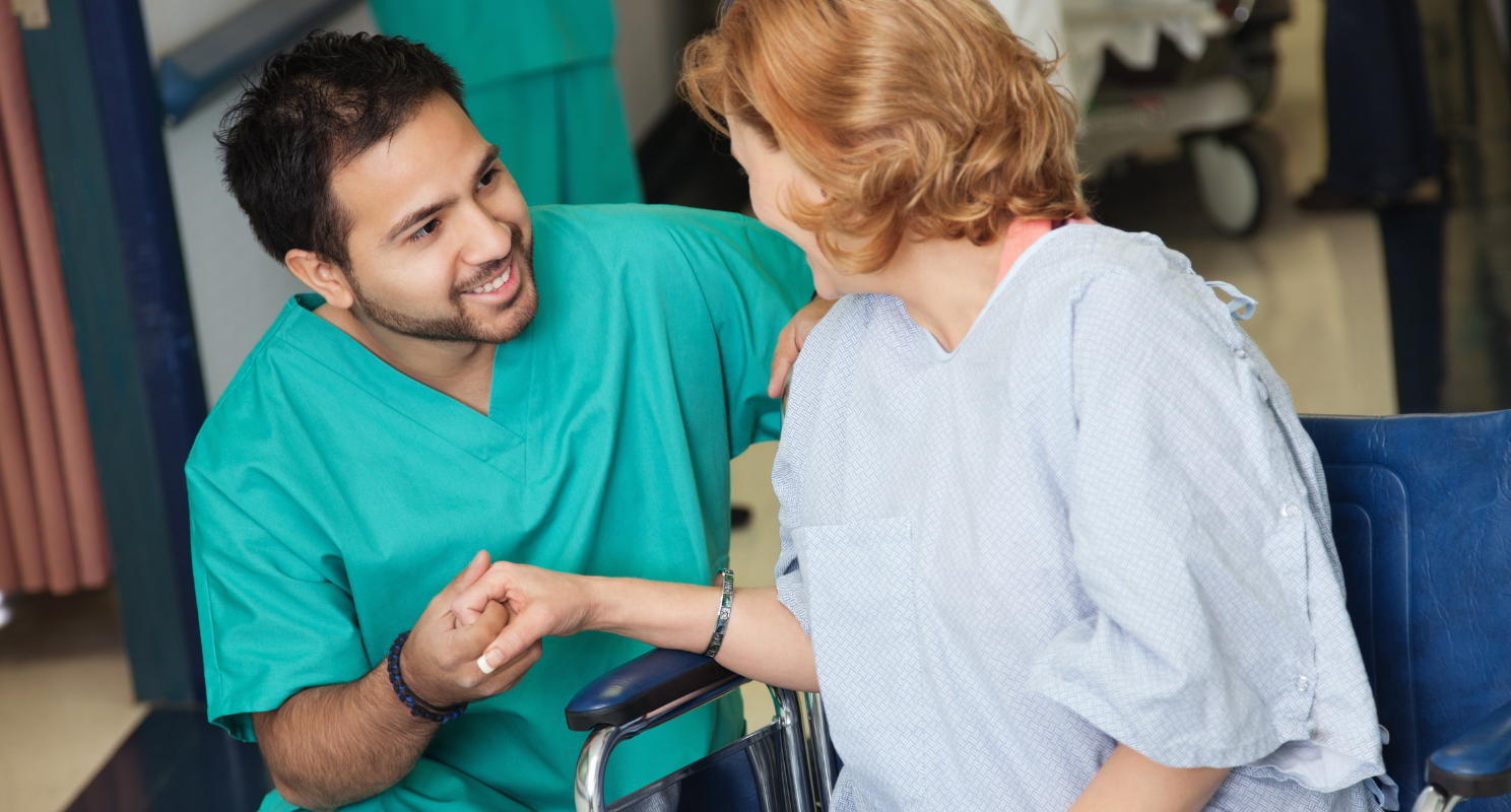 Male nurse, crouching and assisting an elderly blonde woman.