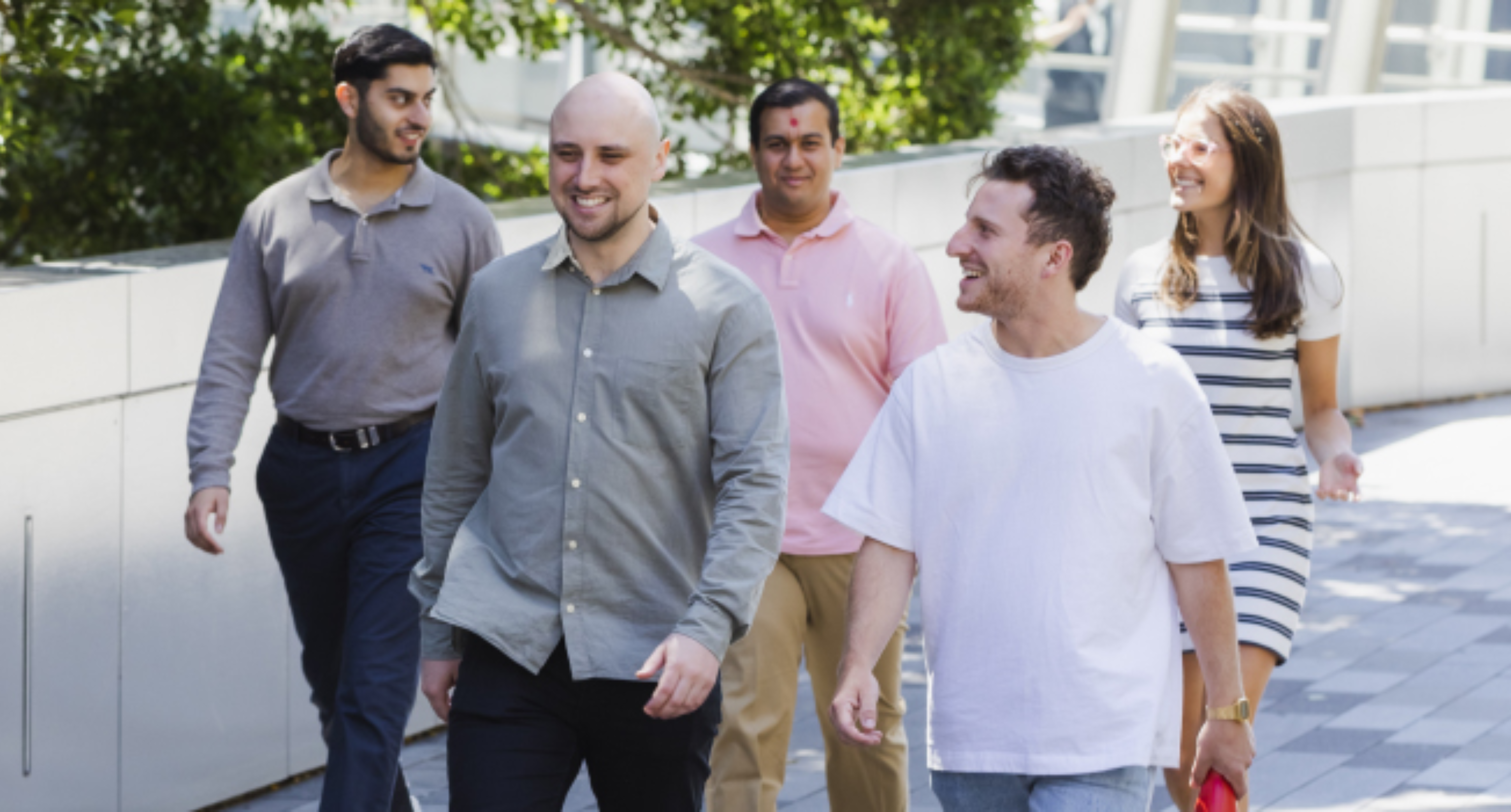 Group of 5 young professionals walking and chatting outside