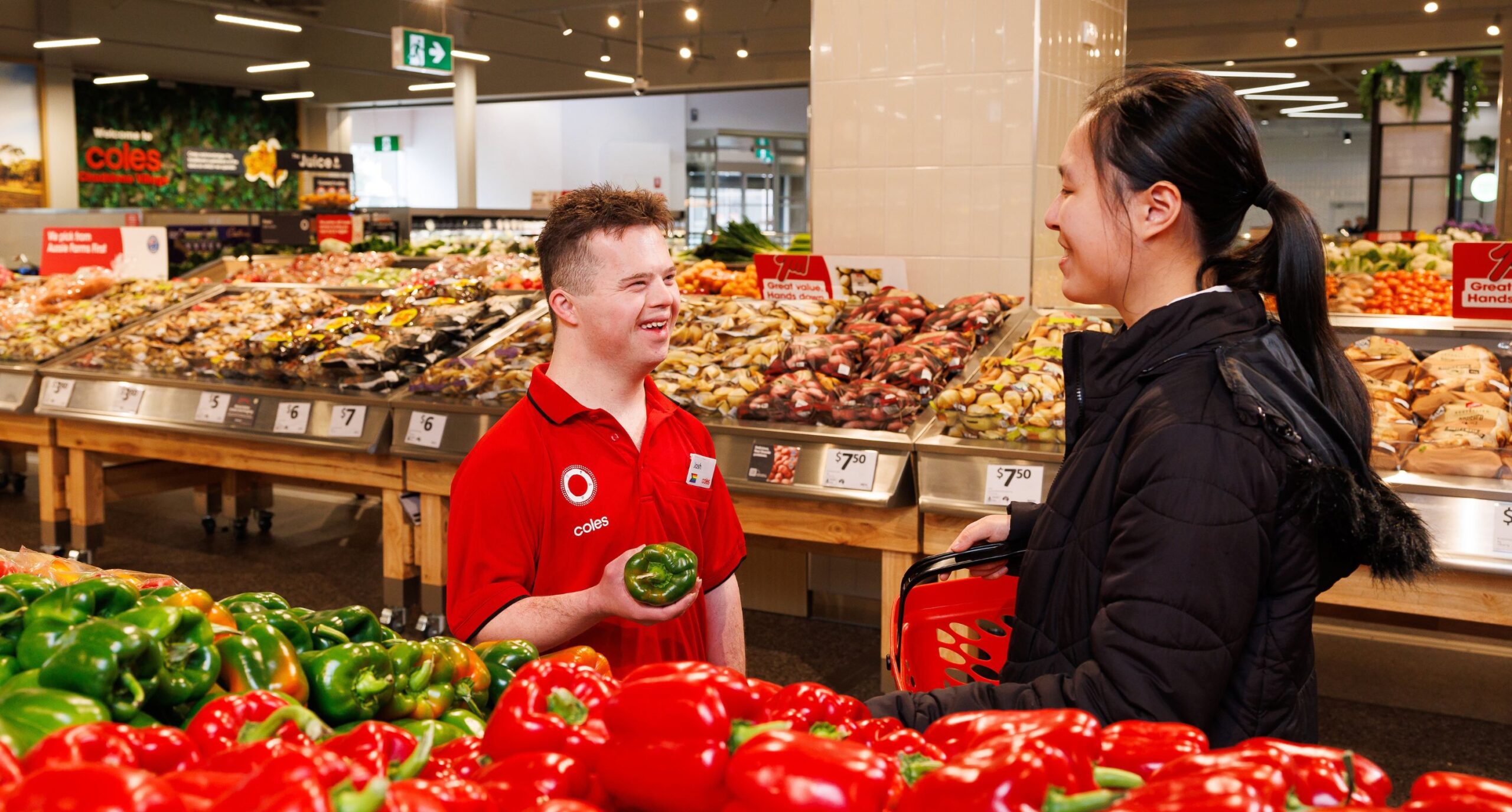 Two Coles employees in uniform, engaging in friendly conversation over fresh vegetables.