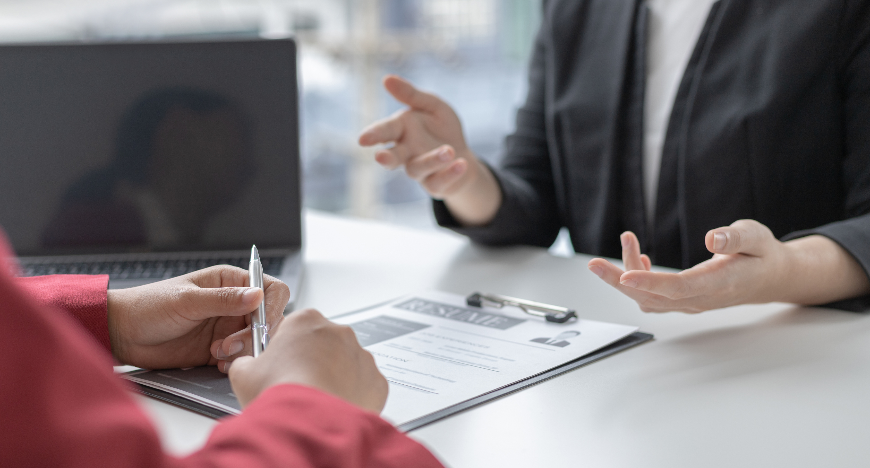 Hiring manager talking to an interviewee over a resume at a desk