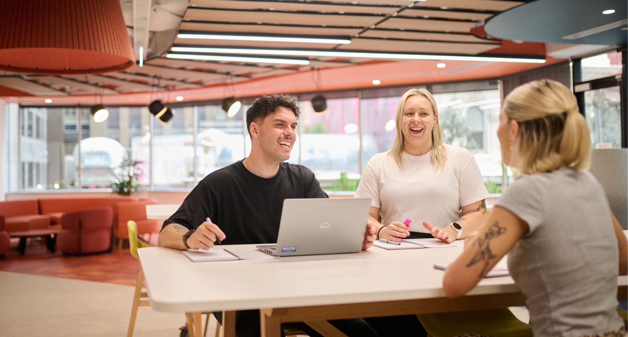 Three young professionals chatting around a table in an office