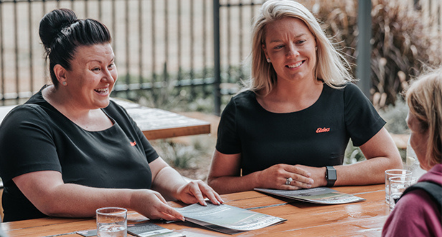 Three Elders professionals in a sit down meeting sat at an outdoor picnic bench