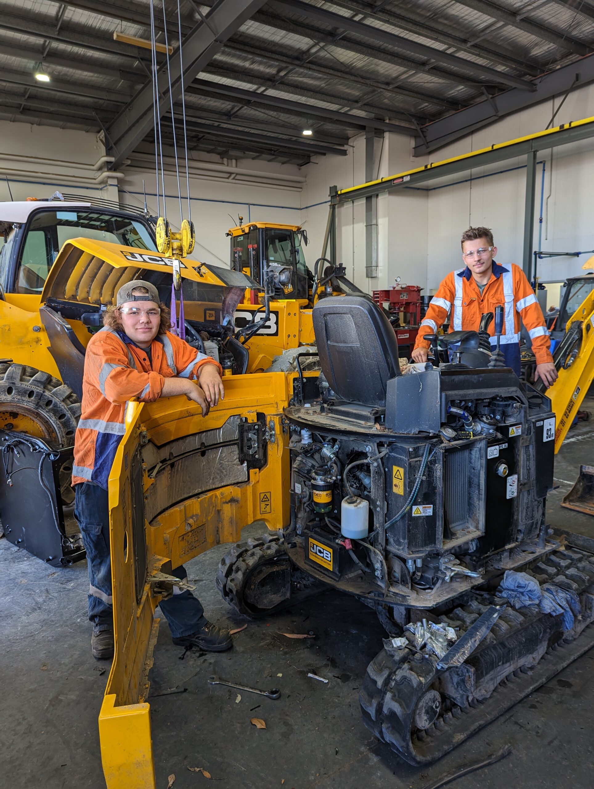 Two male apprentices posing next to JCB construction equipment