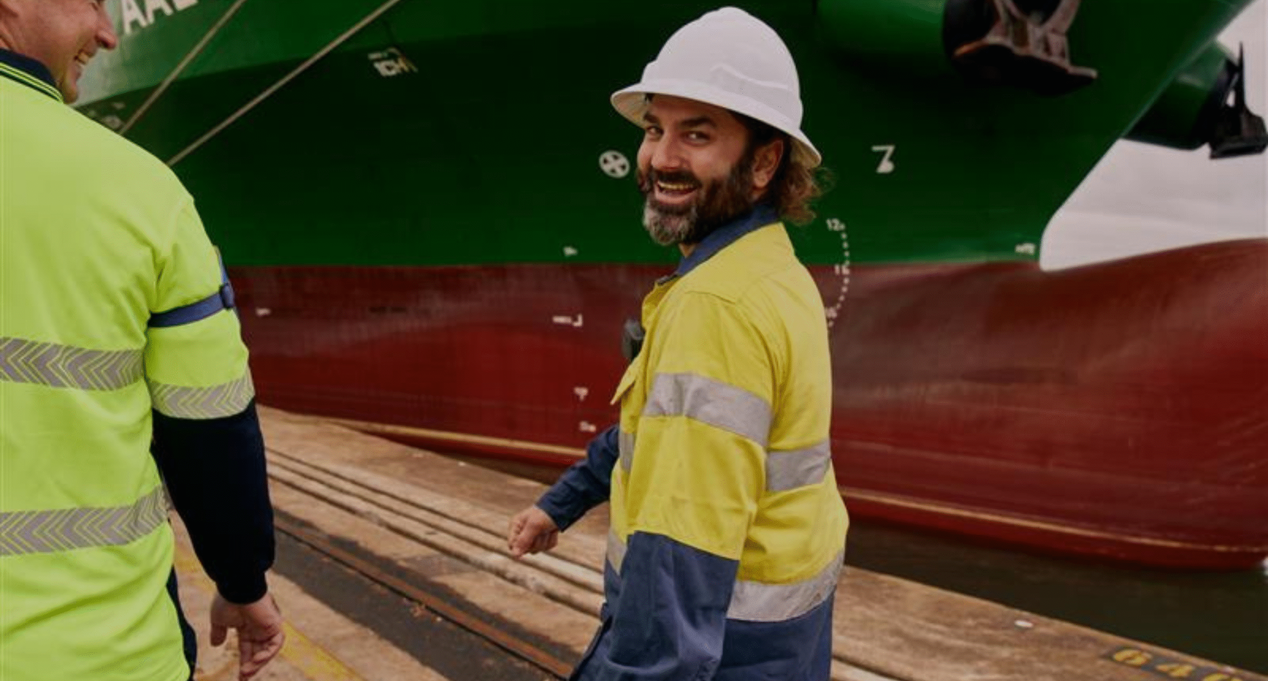 two Qube wharf workers walking next to a ship hull