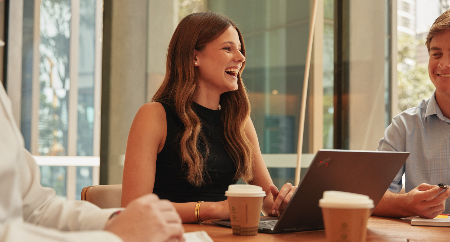 Young female professional, laughing in a team meeting, with coffee cups in the foreground
