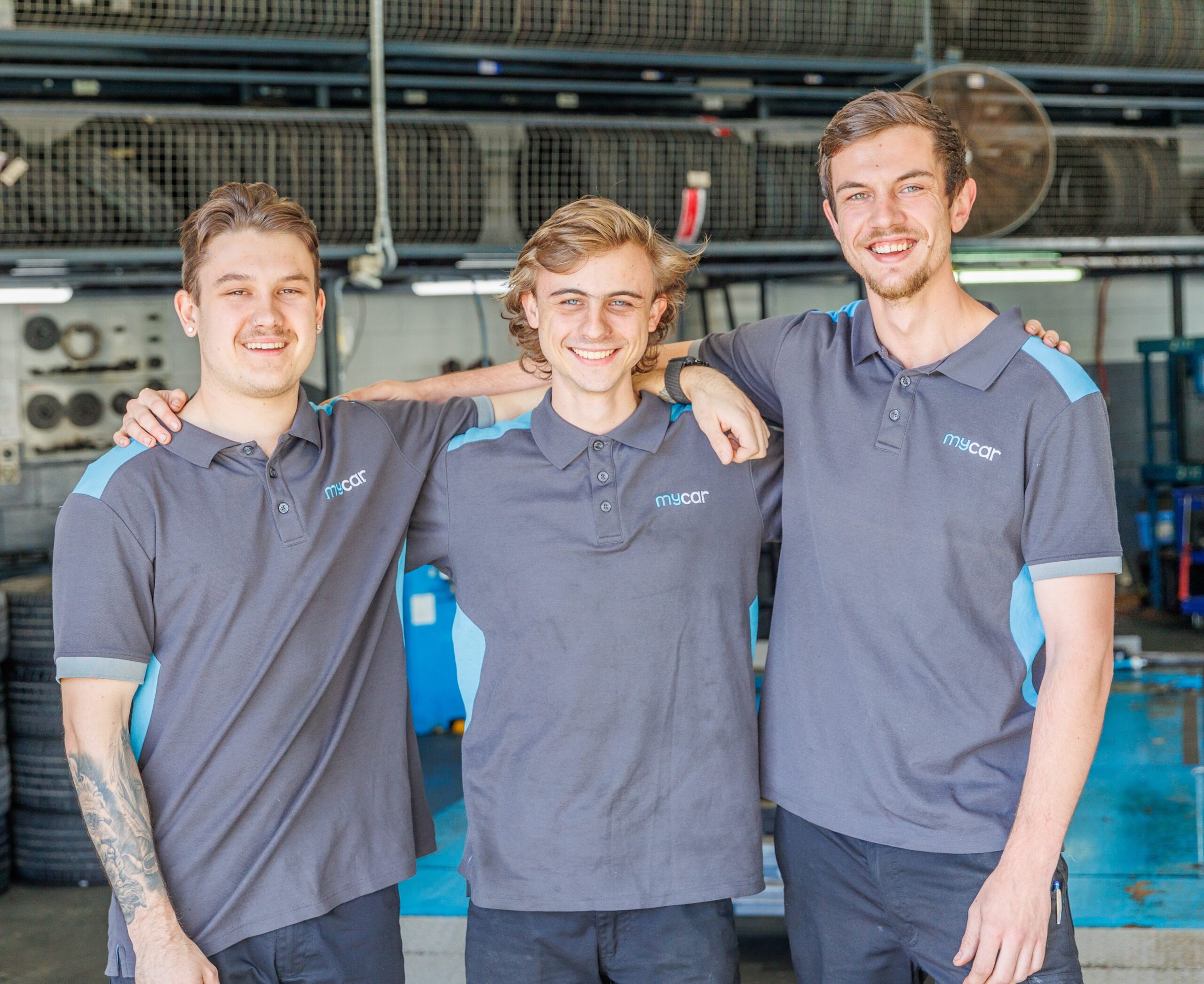 Three young mycar apprentices, smiling with arms round each other's shoulders