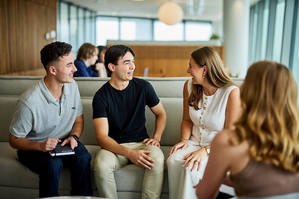 Deloitte graduates, chatting on a sofa in brightly lit, modern office space