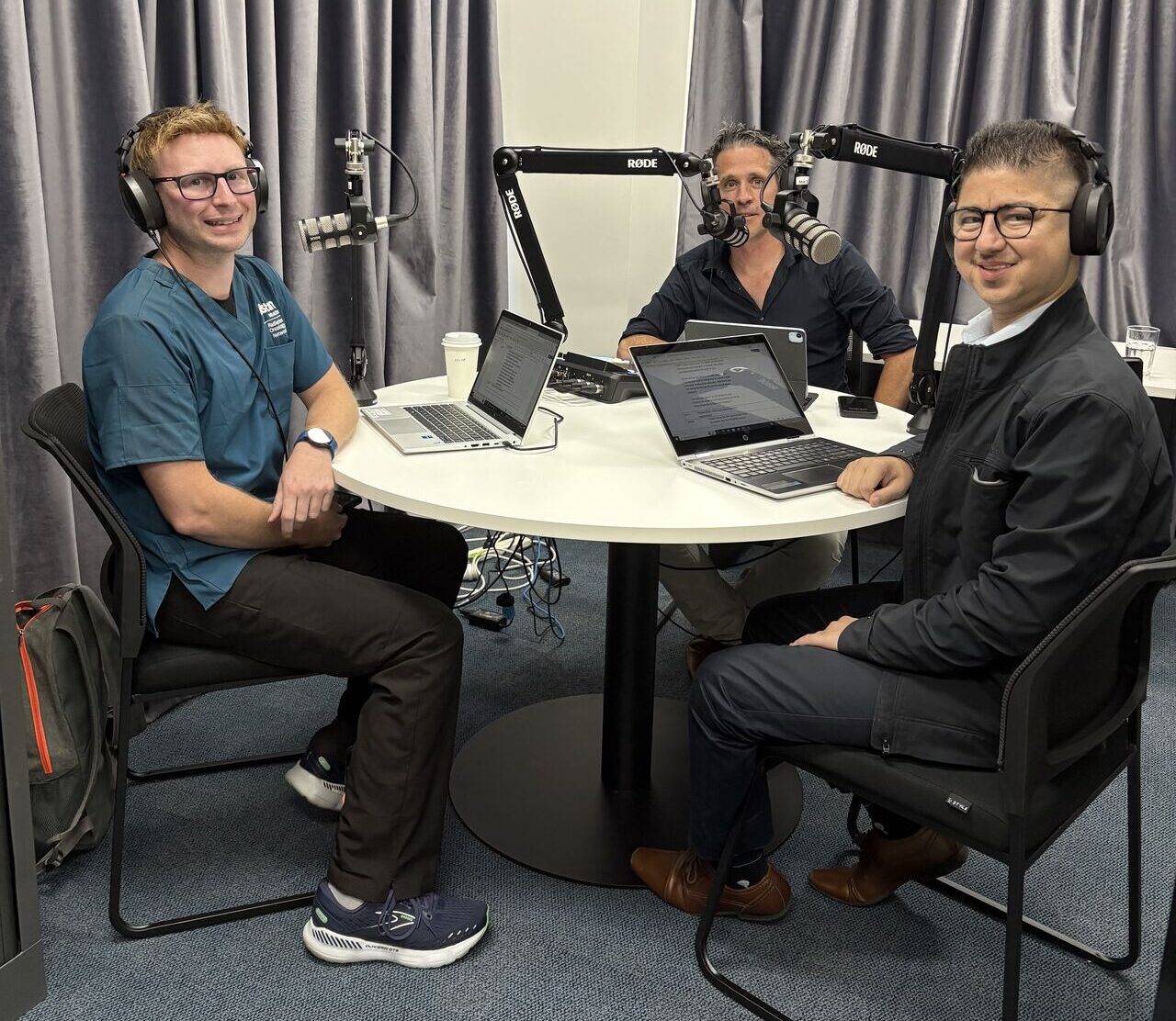 Behind the scenes shot of Karim, Steve, Jarrod wearing headphone speaking into microphones recording the 'Radpod' podcast