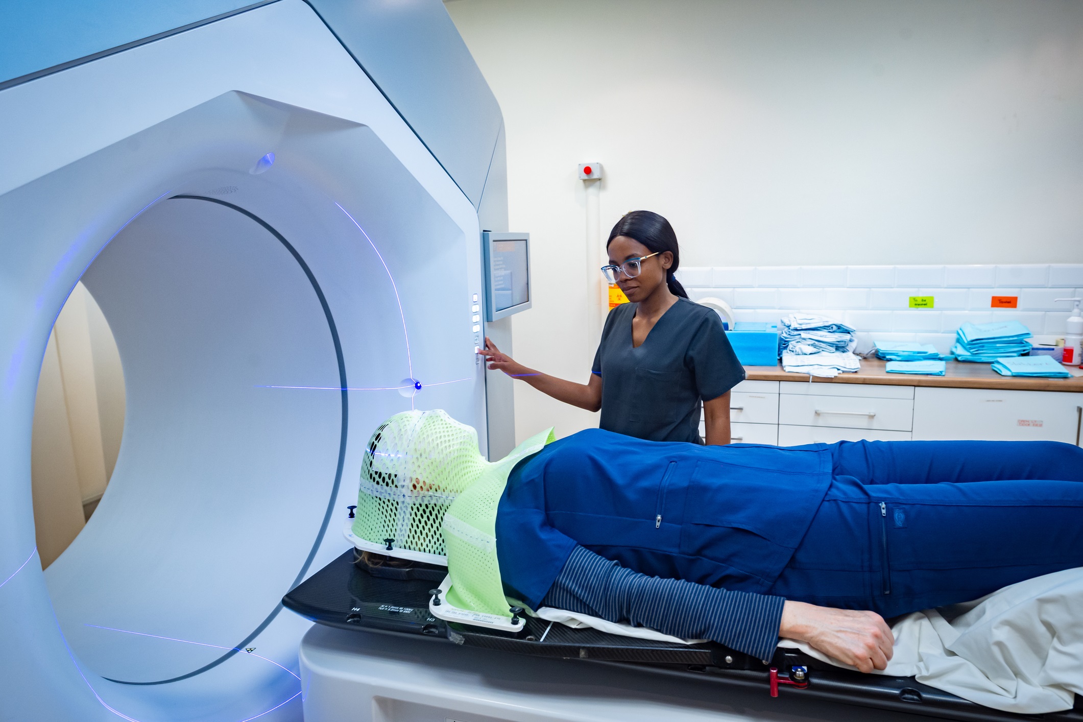 A healthcare worker manages a patient undergoing advanced radiotherapy. The image highlights modern technological advancements in cancer treatment with a linear accelerator. The patient is comfortably positioned with a precision mask for effective therapy delivery, emphasizing medical care and precision.