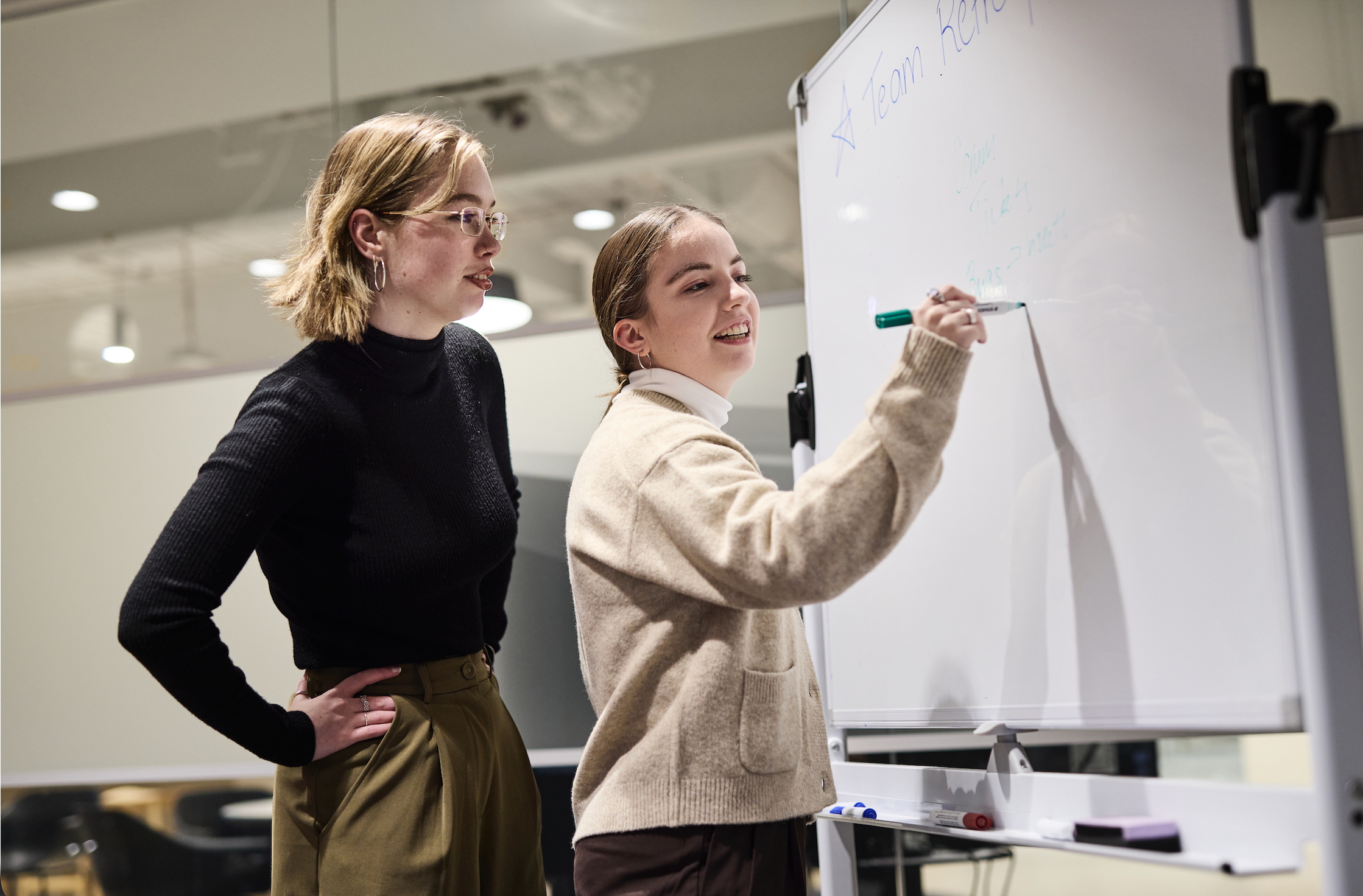 Two young professionals writing on a white board in an office