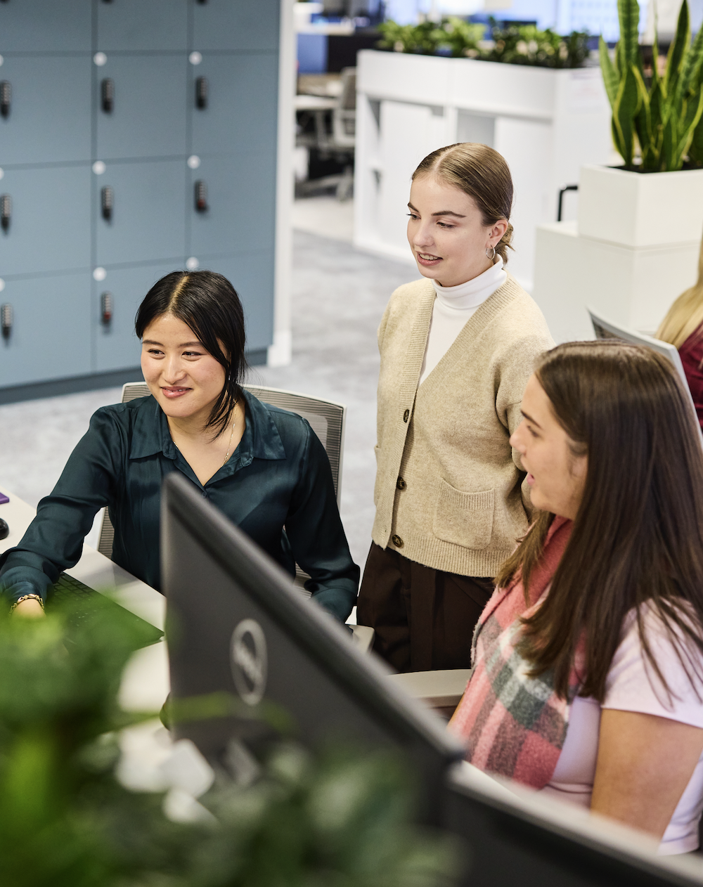 Three female professionals chatting in modern office around a computer